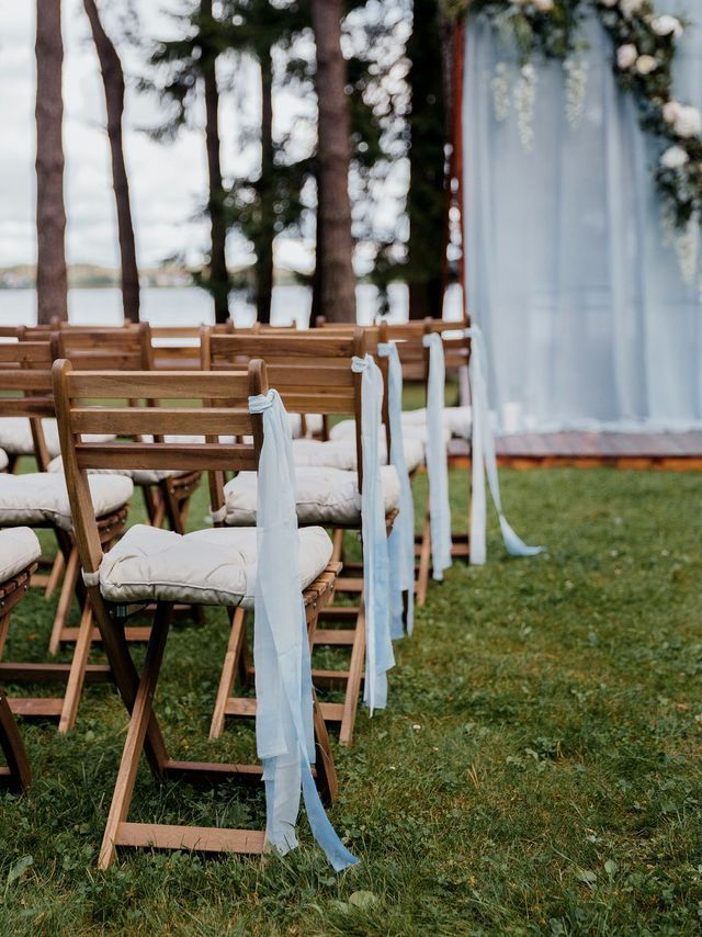 Wooden wedding chairs with blue ribbon ties arranged for coastal ceremony seating at elegant outdoor event with rustic coastal décor