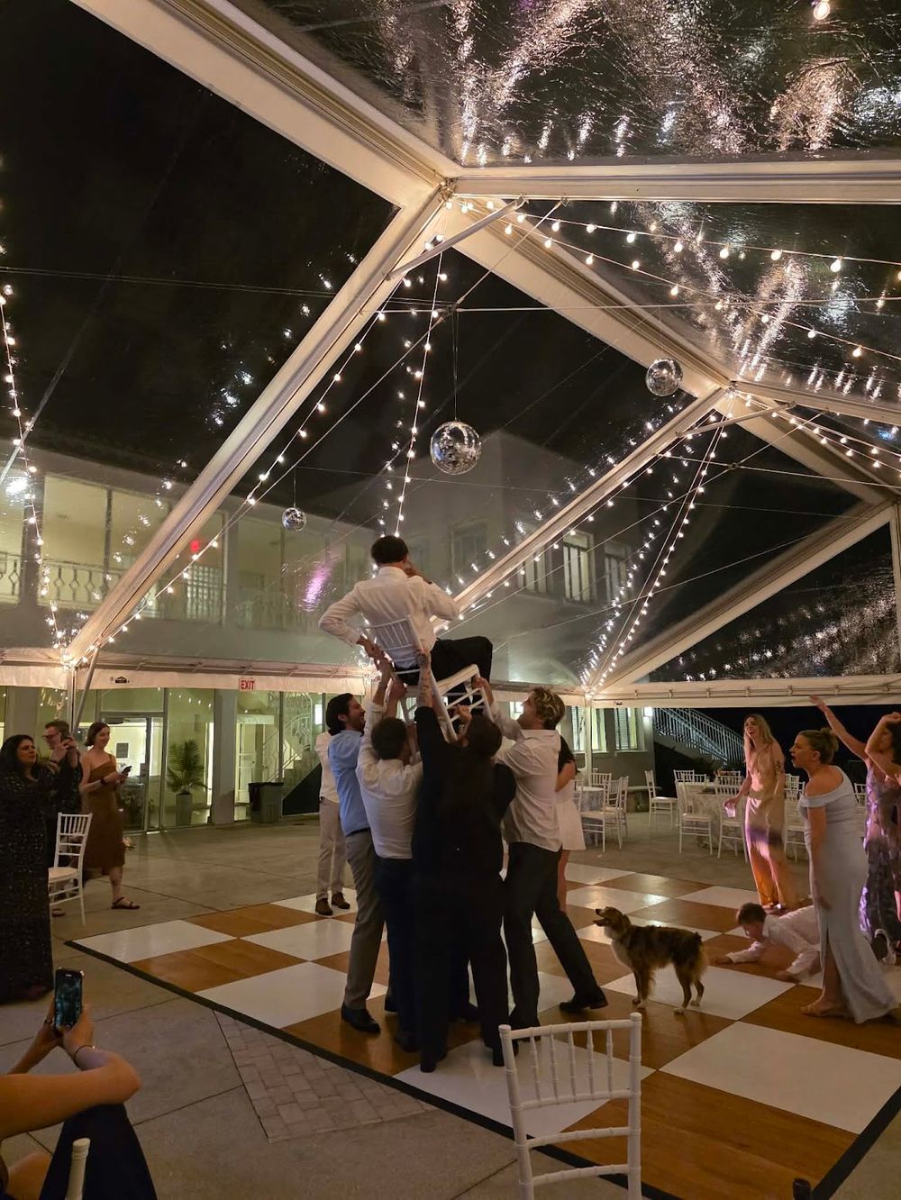 Groom hoisted in chair at eclectic wedding ceremony with hanging disco balls and modern luxury rental décor and celebration styling setup