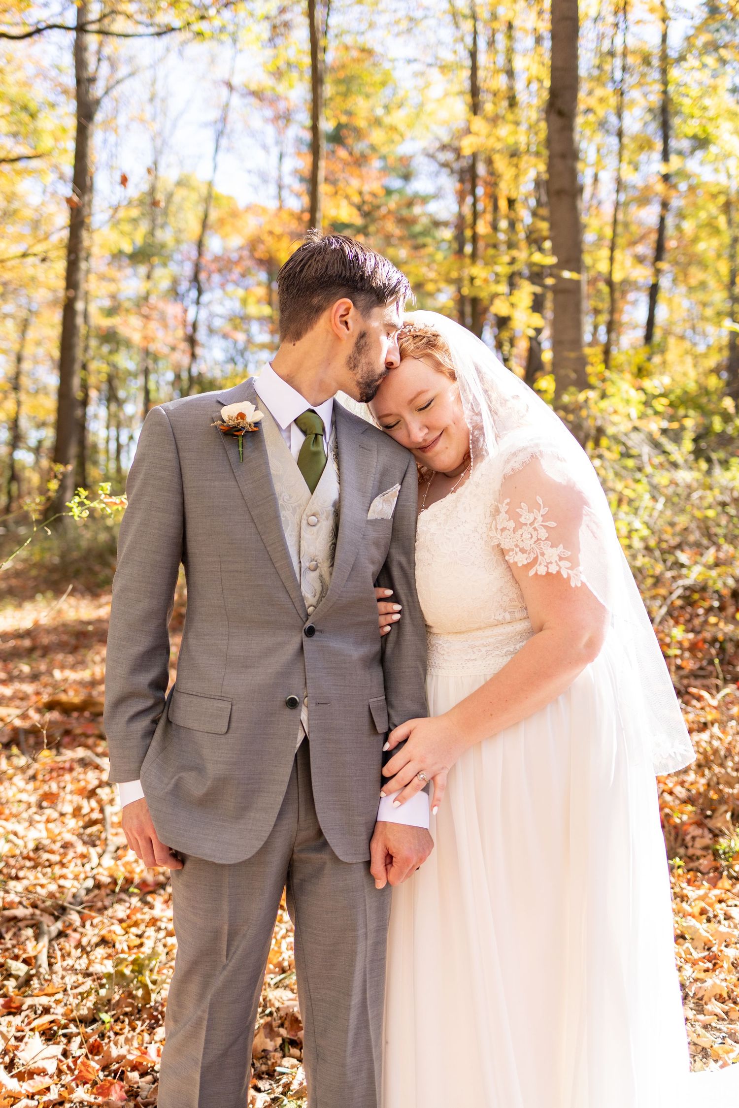 Bride and groom embrace in autumn forest, she leans on his shoulder in lace gown and veil, he wears gray suit. Cincinnati Elopement Photo