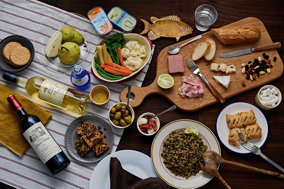 Overhead view of elegant charcuterie spread with wine, cheese, vegetables, bread and mixed dishes on wooden boards.