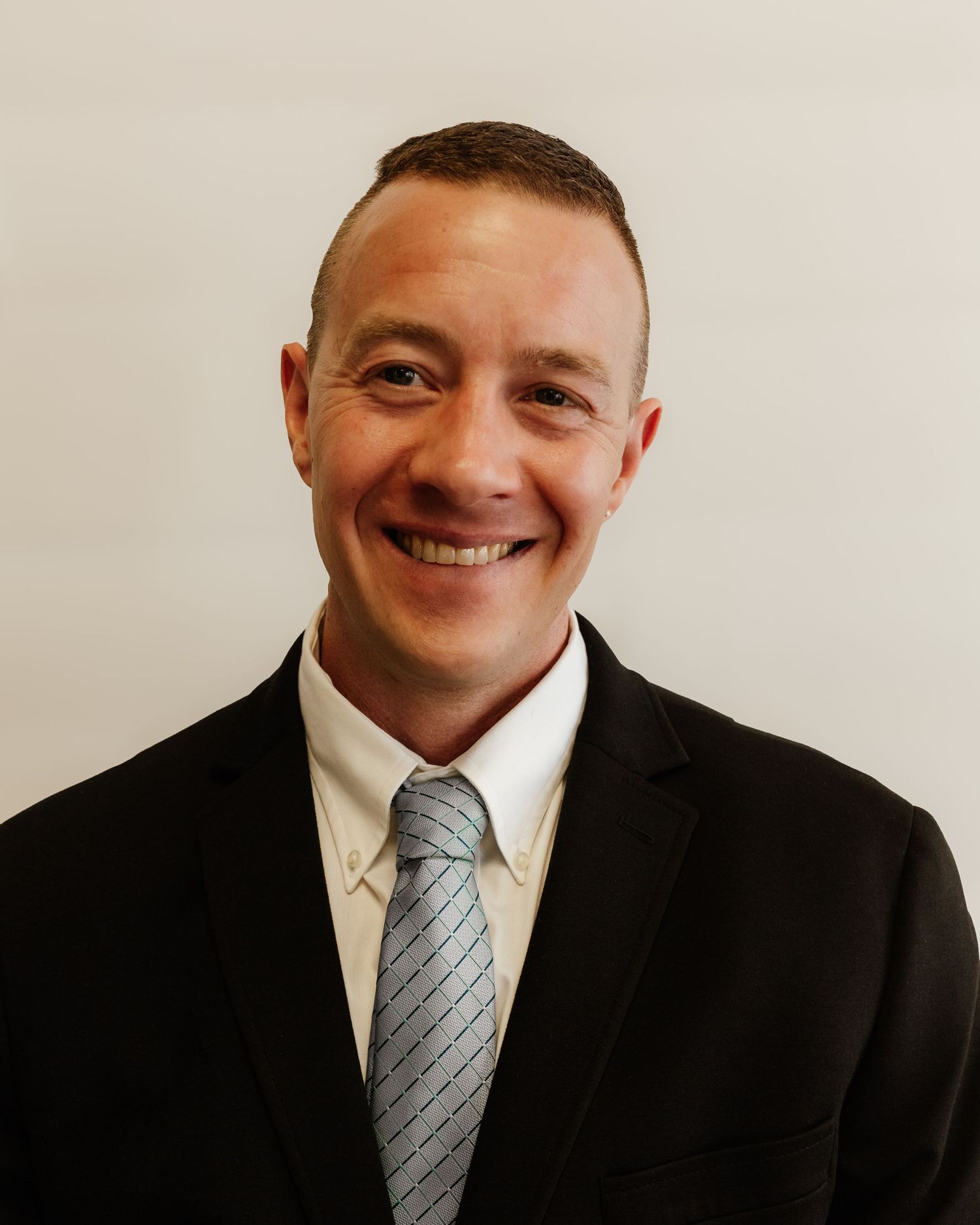 Professional headshot of a smiling man in a black suit and gray striped tie against a white background.