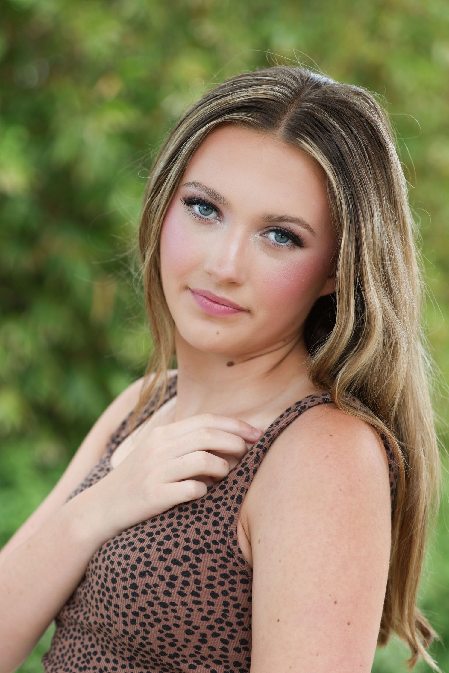 Person in animal print tank top and black athletic pants poses outdoors against green foliage background.