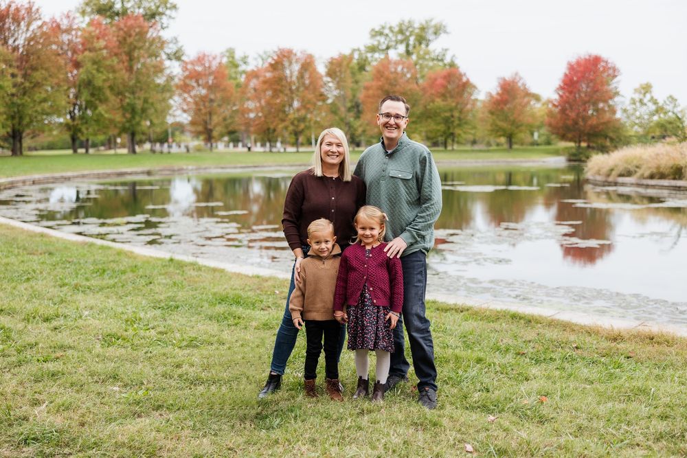Family enjoying autumn scenery by a lake with colorful fall foliage in the background.