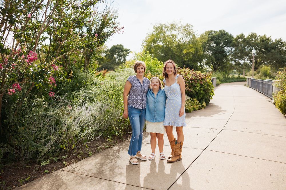 People walking together on a sunny pathway lined with flowering bushes.