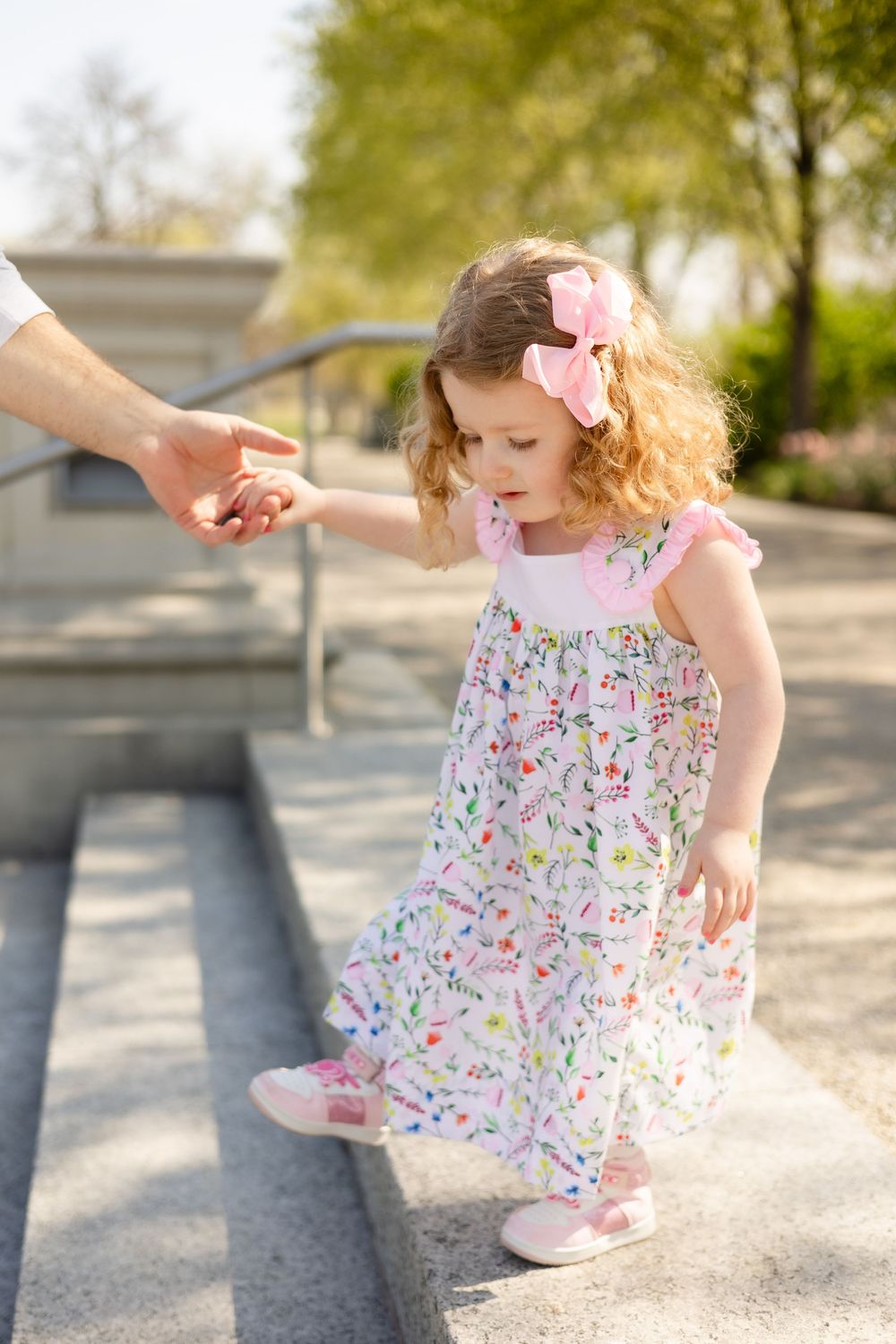 Child in floral dress twirling and dancing on a sunny pathway.