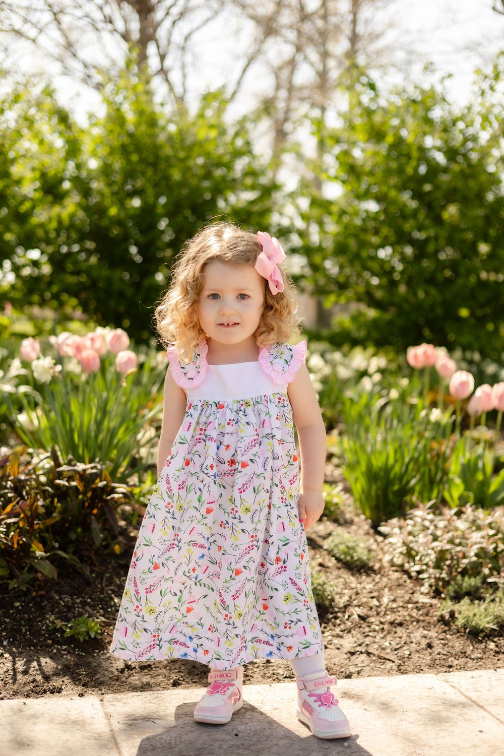 A child in floral dress poses near blooming tulips in a spring garden.