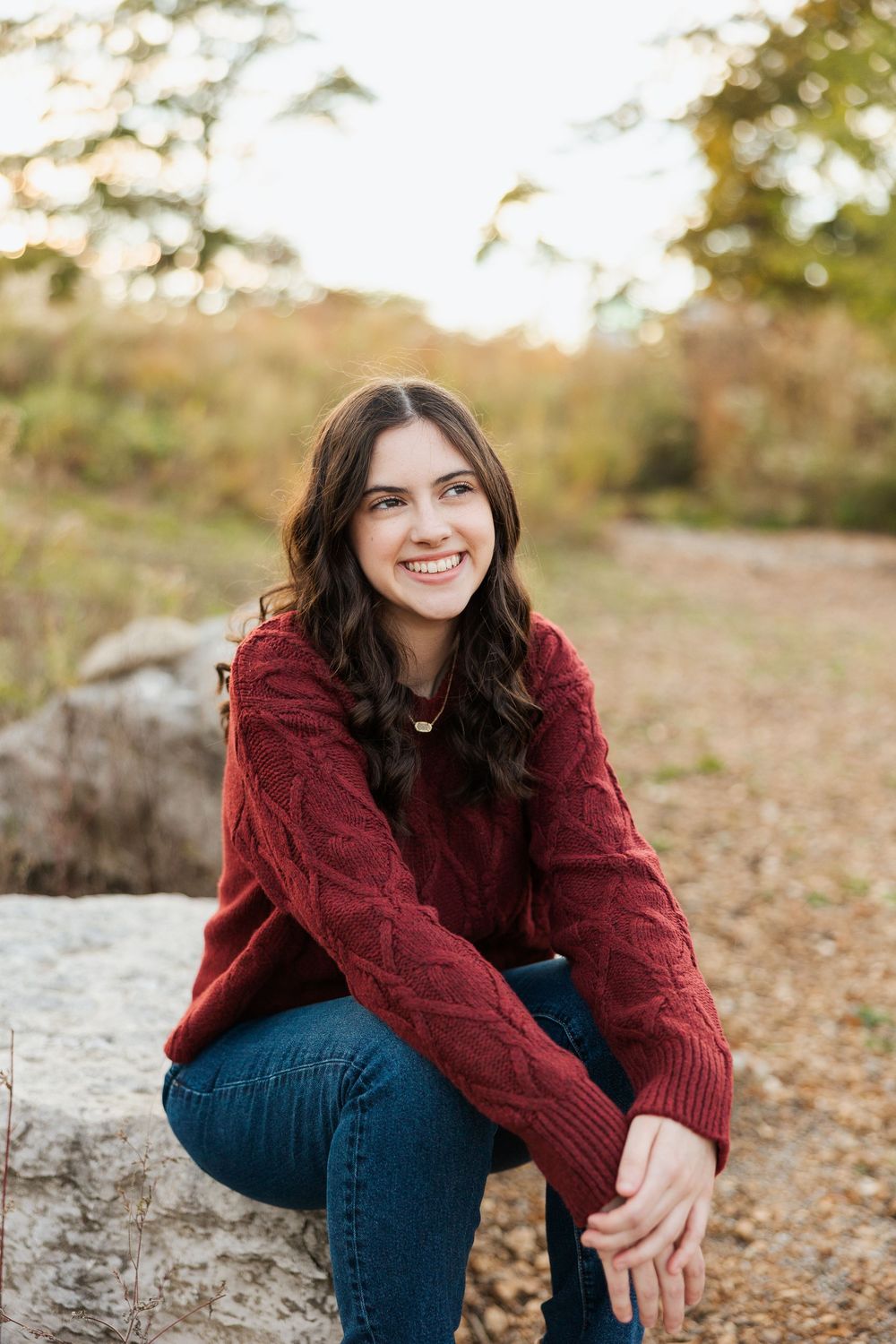 Person in burgundy sweater sitting casually on rocks during autumn photoshoot.
