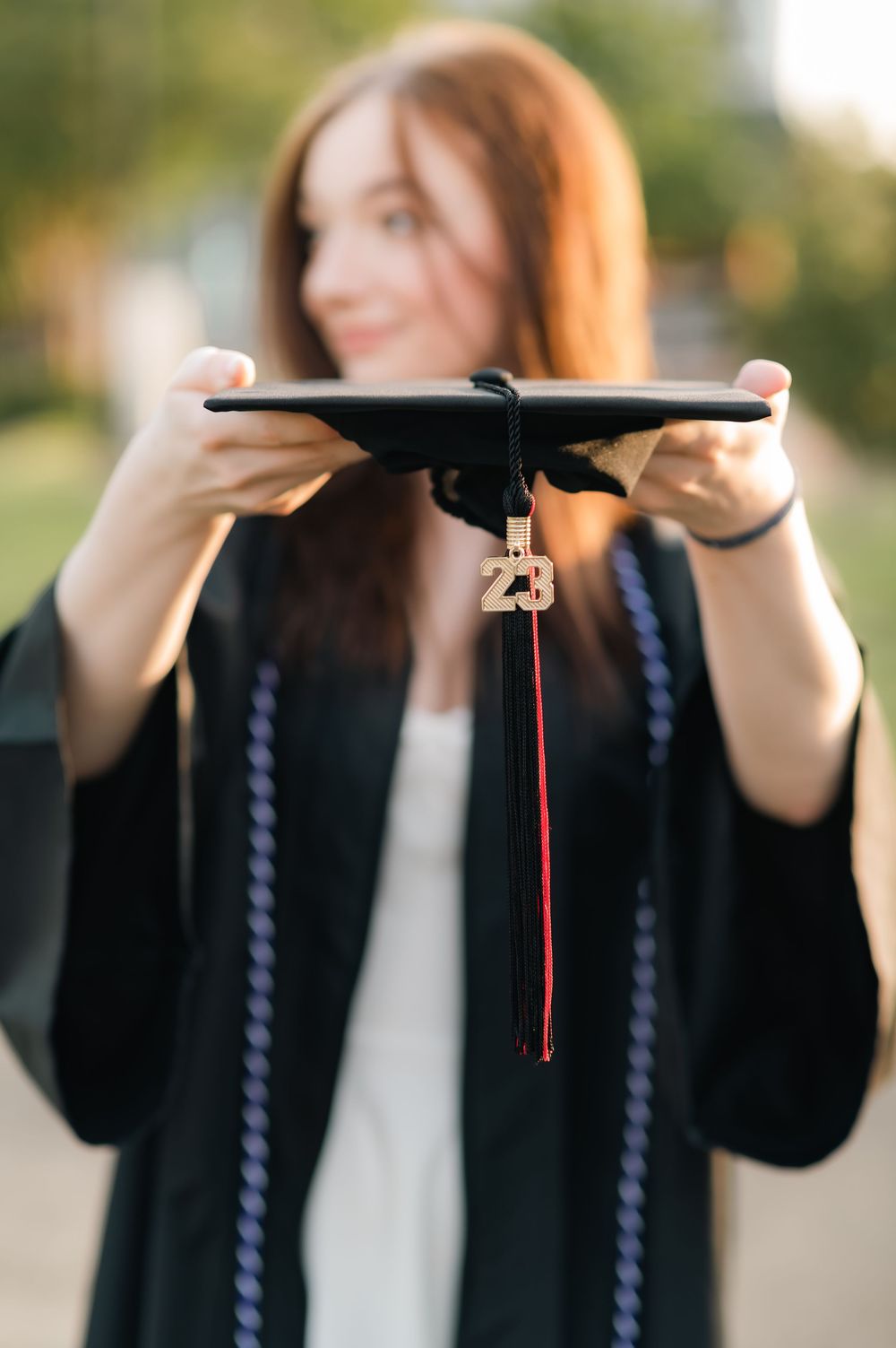 Graduate holding diploma and smiling while wearing black graduation gown outdoors.