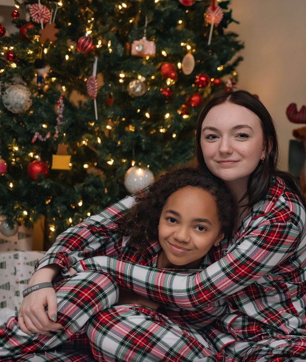 Two people in matching plaid Christmas pajamas posing in front of decorated tree.
