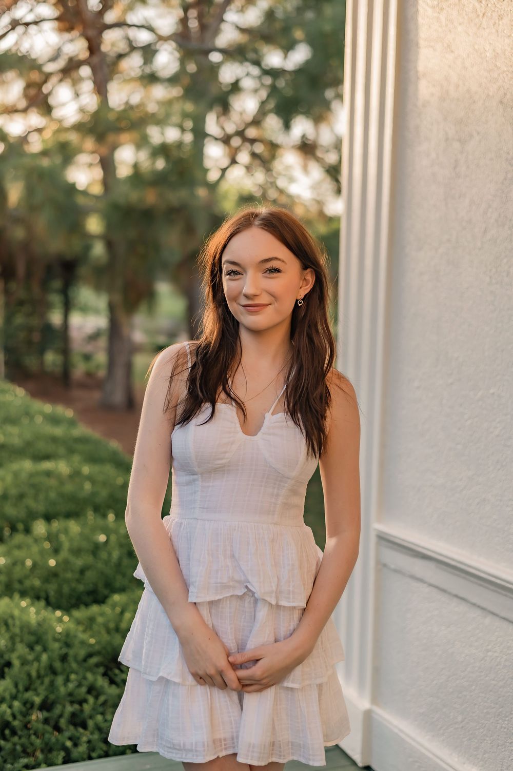 Portrait of young woman in white summer dress standing by column outdoors.