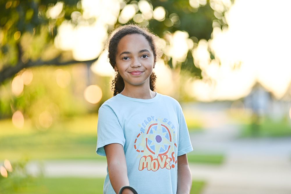 Child wearing light blue t-shirt with donut design smiling outdoors at sunset.