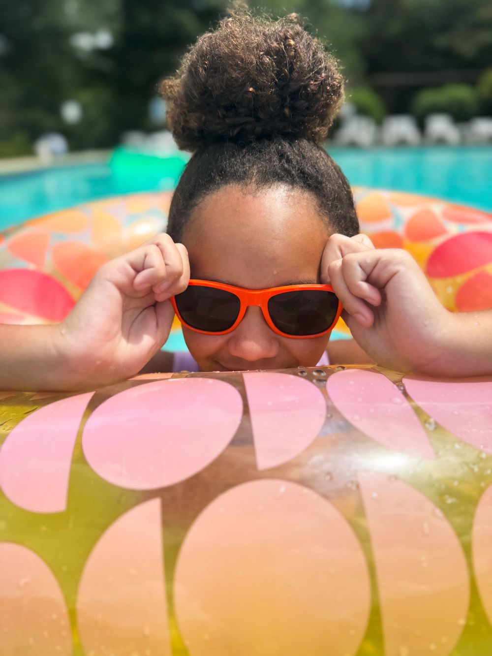 Person peeking over pool float while wearing orange sunglasses on a sunny summer day.