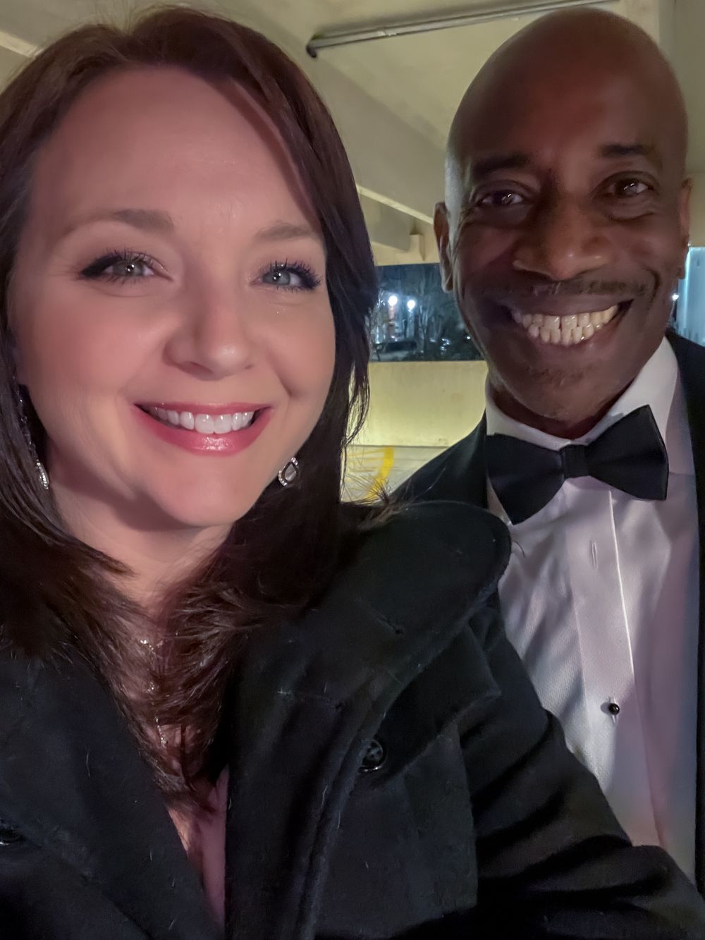 Two people in formal attire taking selfie at evening event.