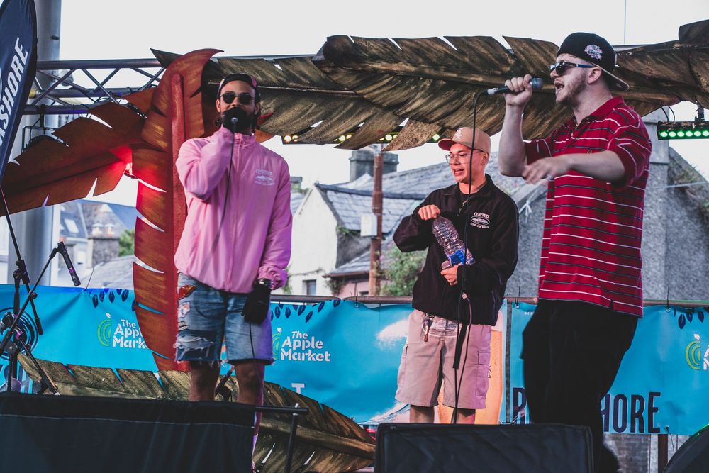 A group of people gather at an outdoor event with blue banners visible in the background.