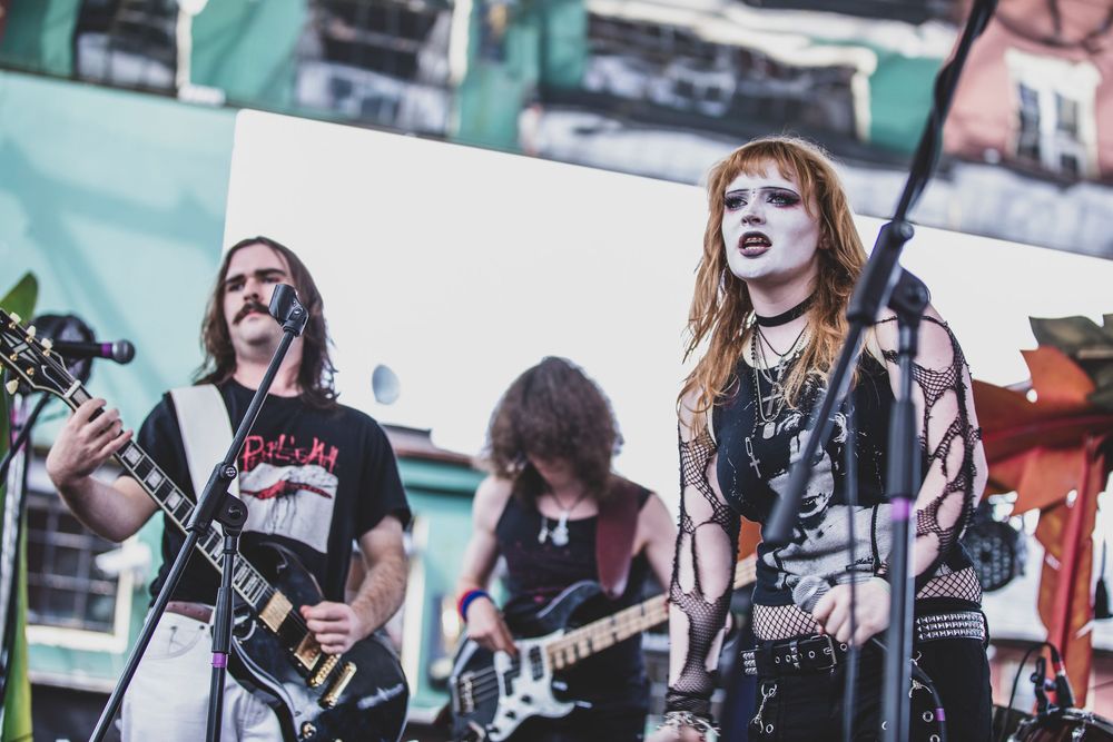 Heavy metal musicians perform on stage with guitars and microphones during an energetic outdoor concert performance.