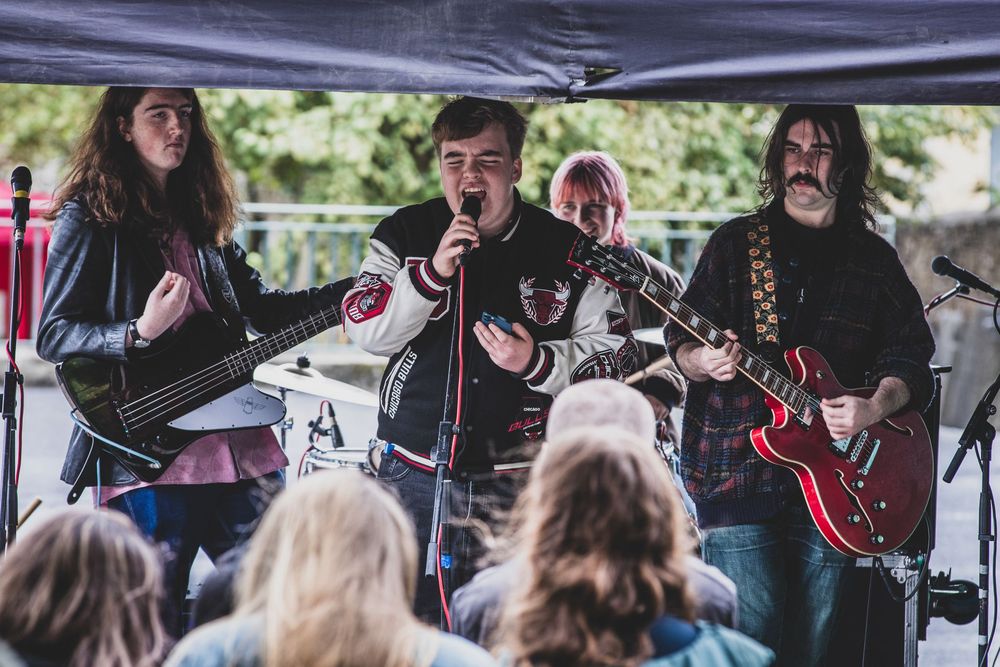 Musicians perform together outdoors under a tent canopy during a live event.