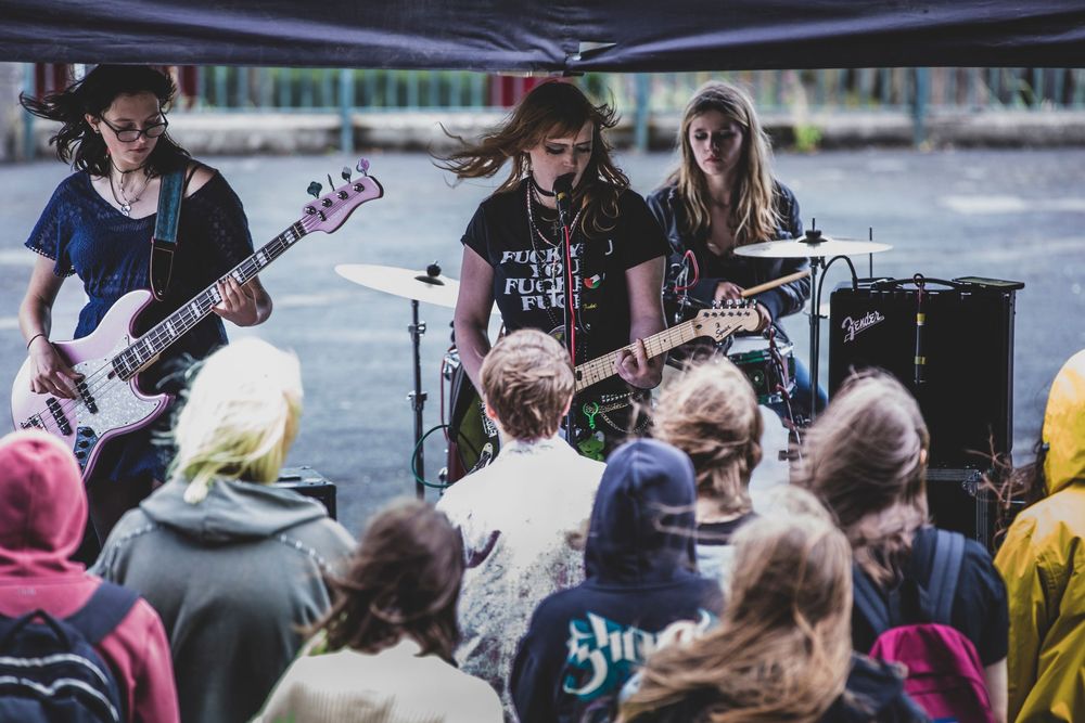 Musicians perform on stage at an outdoor concert venue with guitars and instruments by the water.