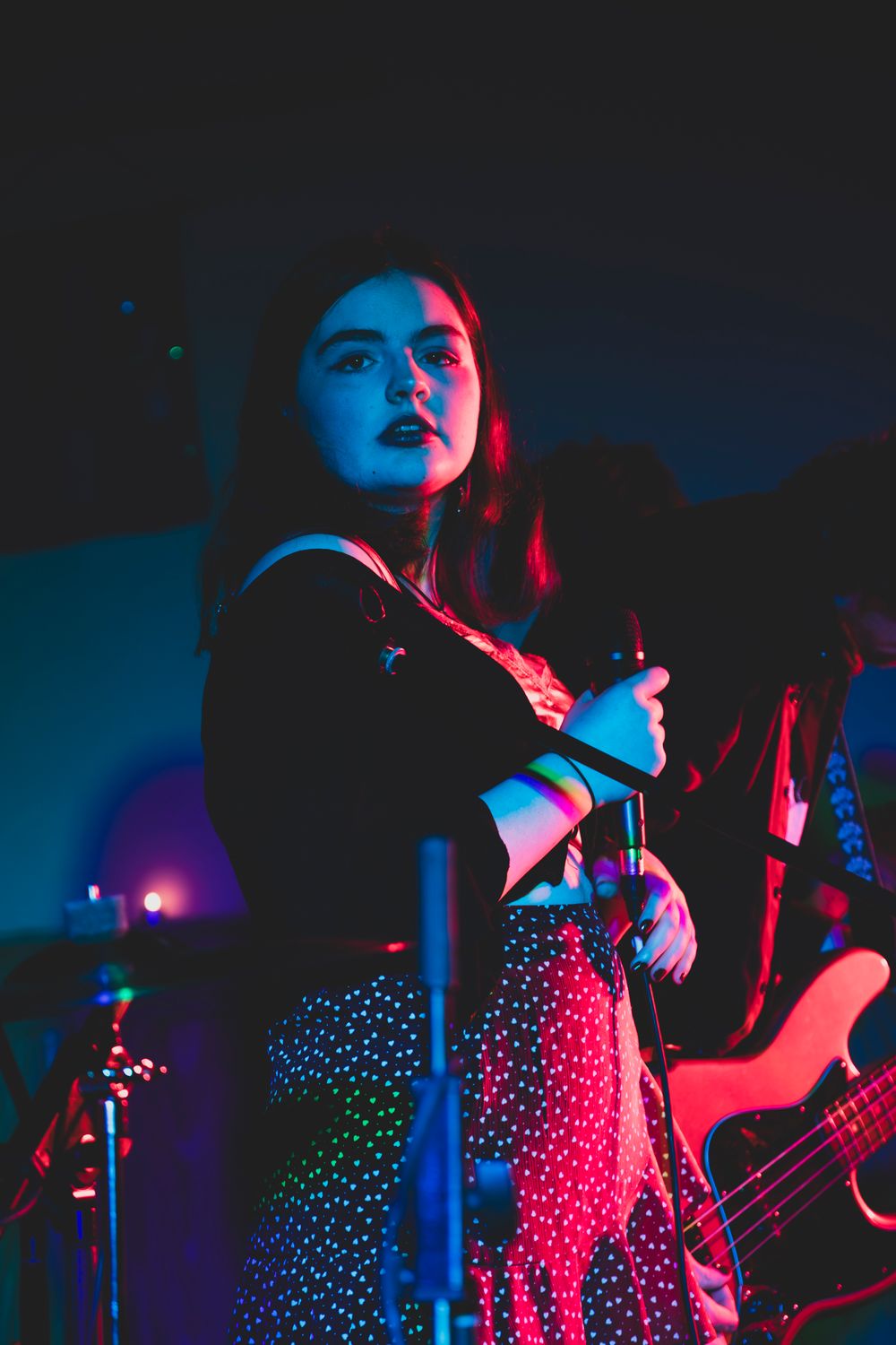 Atmospheric concert photo of a performer in a polka dot dress illuminated by dramatic blue and red stage lighting.