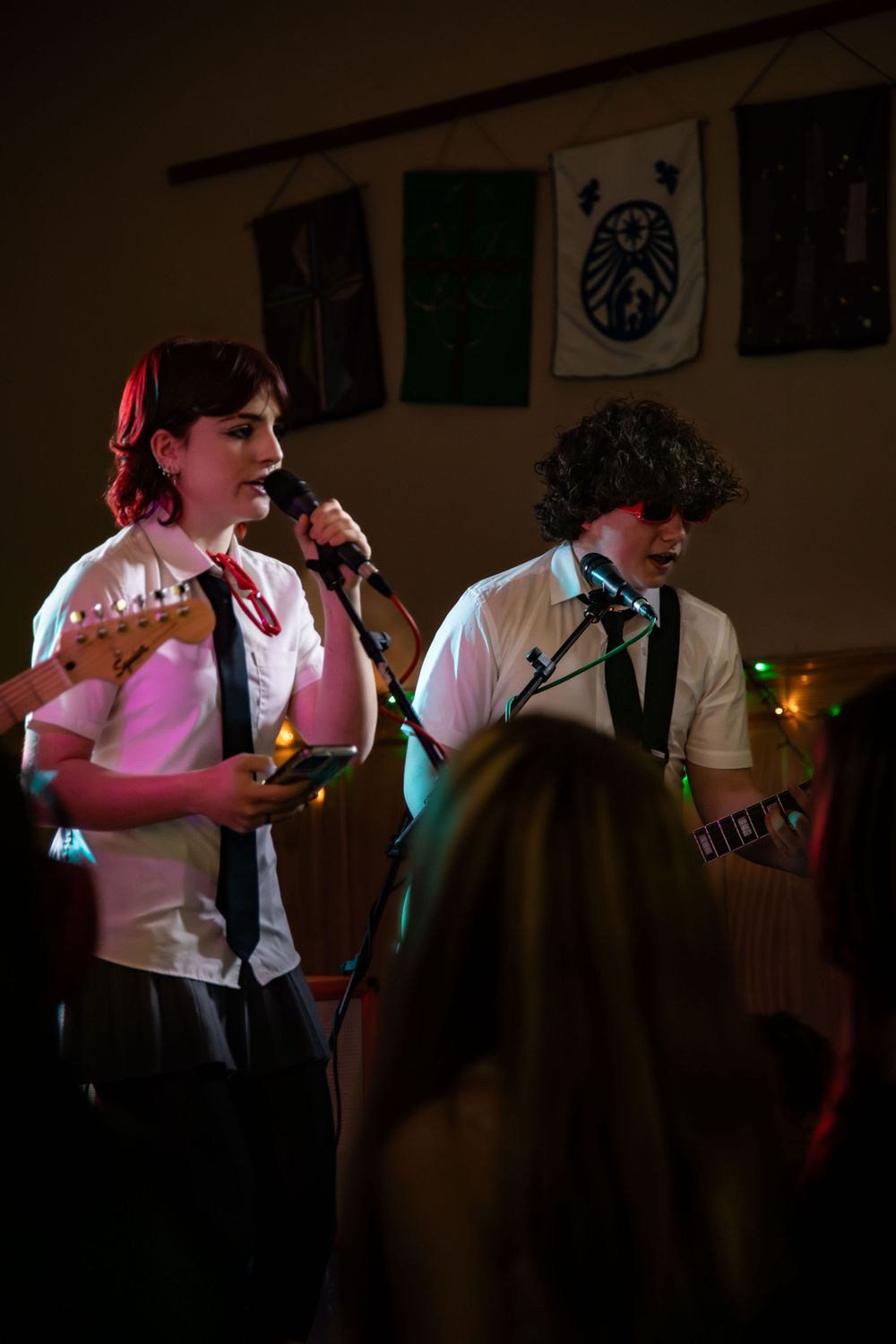 Musicians in white shirts perform on stage with microphones and instruments under moody lighting at a small venue.