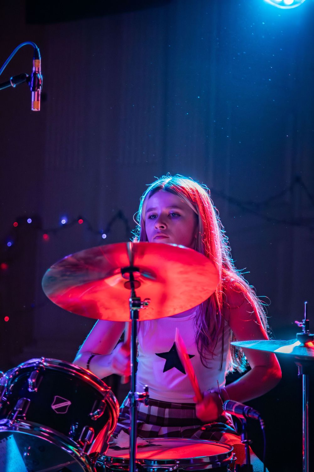 Drummer performing on stage illuminated by dramatic red and blue lighting during a concert performance.
