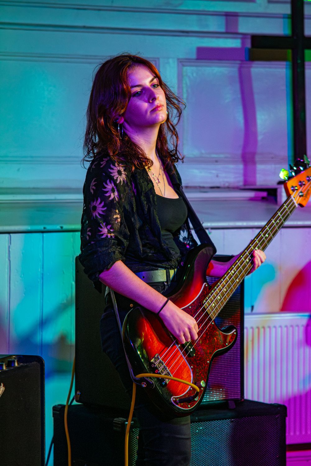 A musician performs with a bass guitar under vibrant turquoise and purple stage lighting.