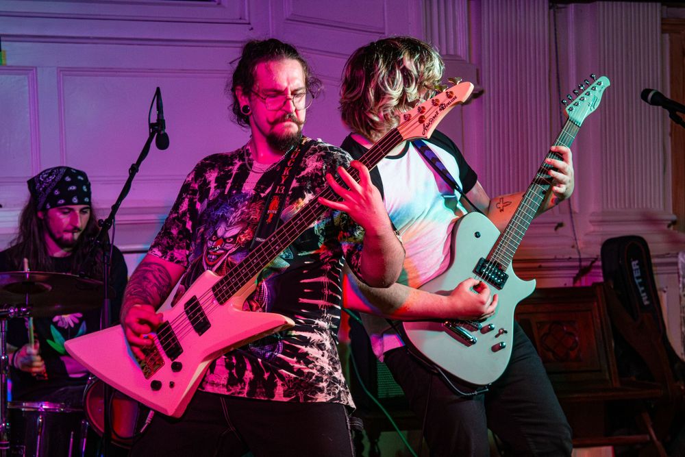 Musicians perform on stage with electric guitars under dramatic red and blue lighting at a live concert.