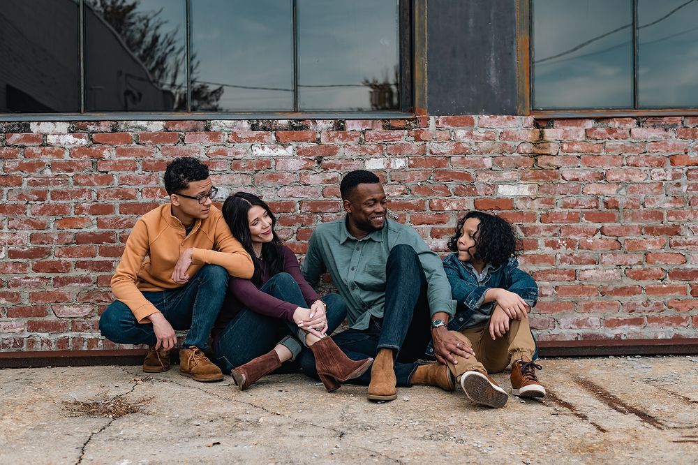 A family sits casually together against a brick wall sharing a relaxed moment.