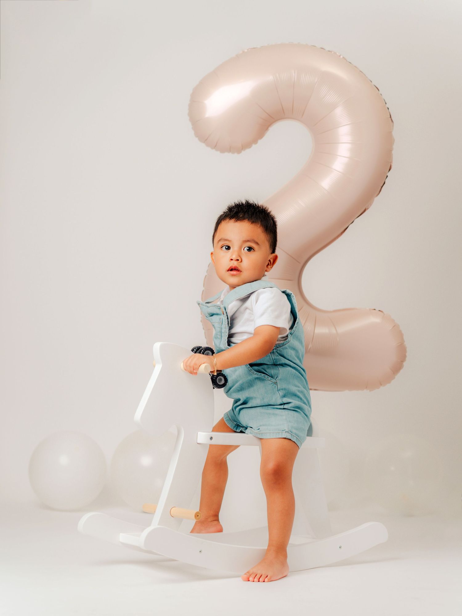 A series of four photos showing a small child sitting and playing on a large pink inflatable number 2 balloon decoration.