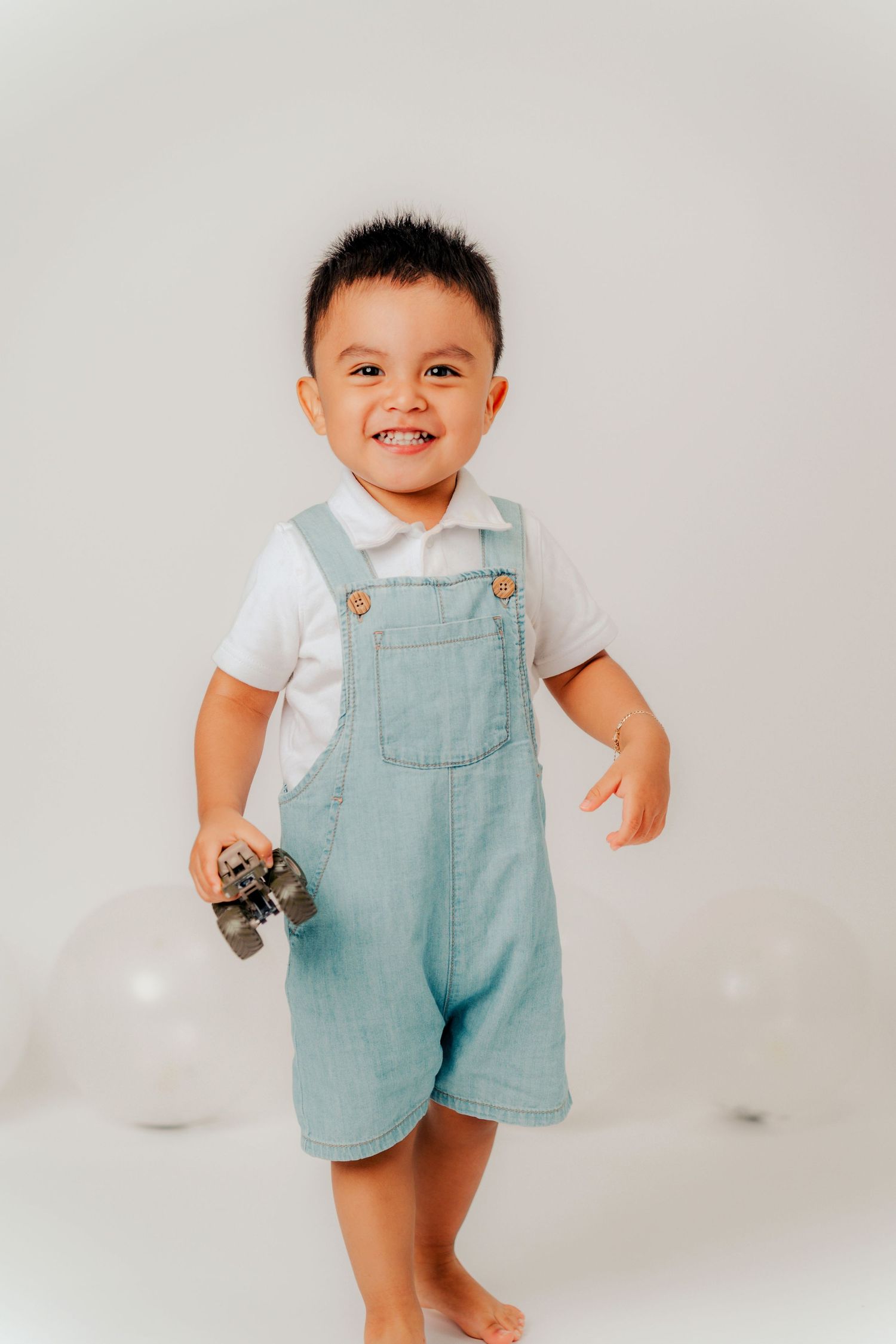 Baby wearing light blue overalls and white shirt smiles while standing against white background in three poses.