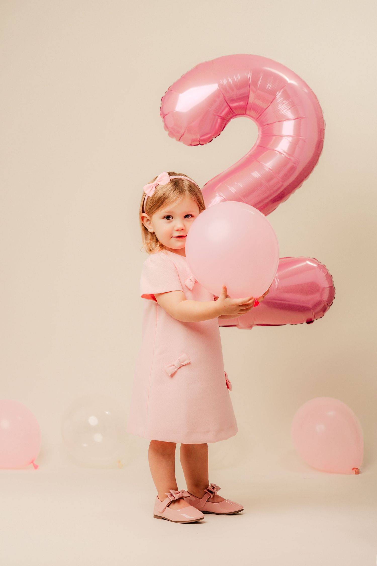 Pink birthday celebration setup with large number 2 balloon and small pink balloons against beige backdrop.