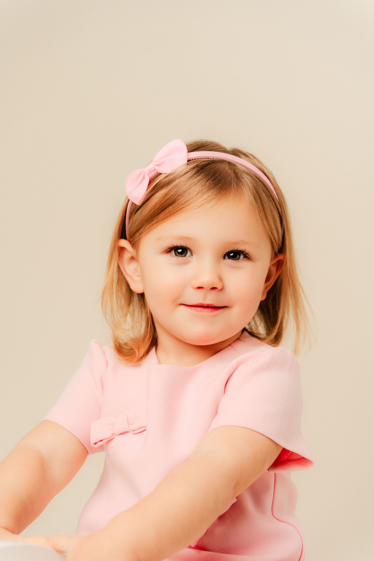 Three connected photos show a young child in a pink dress and bow against a light background.