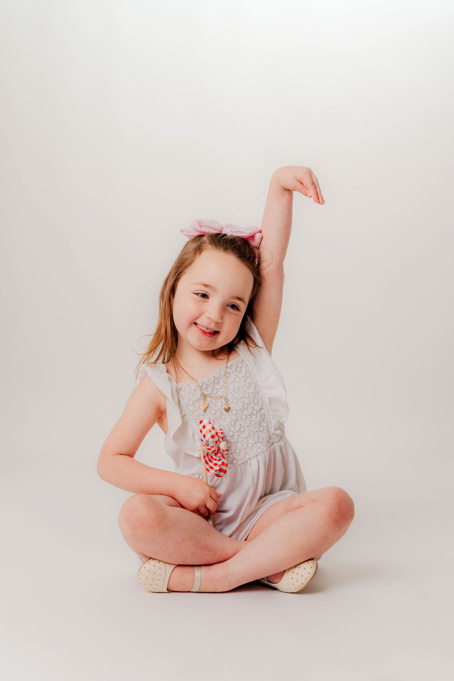 Young child in a grey dress poses playfully while sitting cross-legged on a white backdrop.