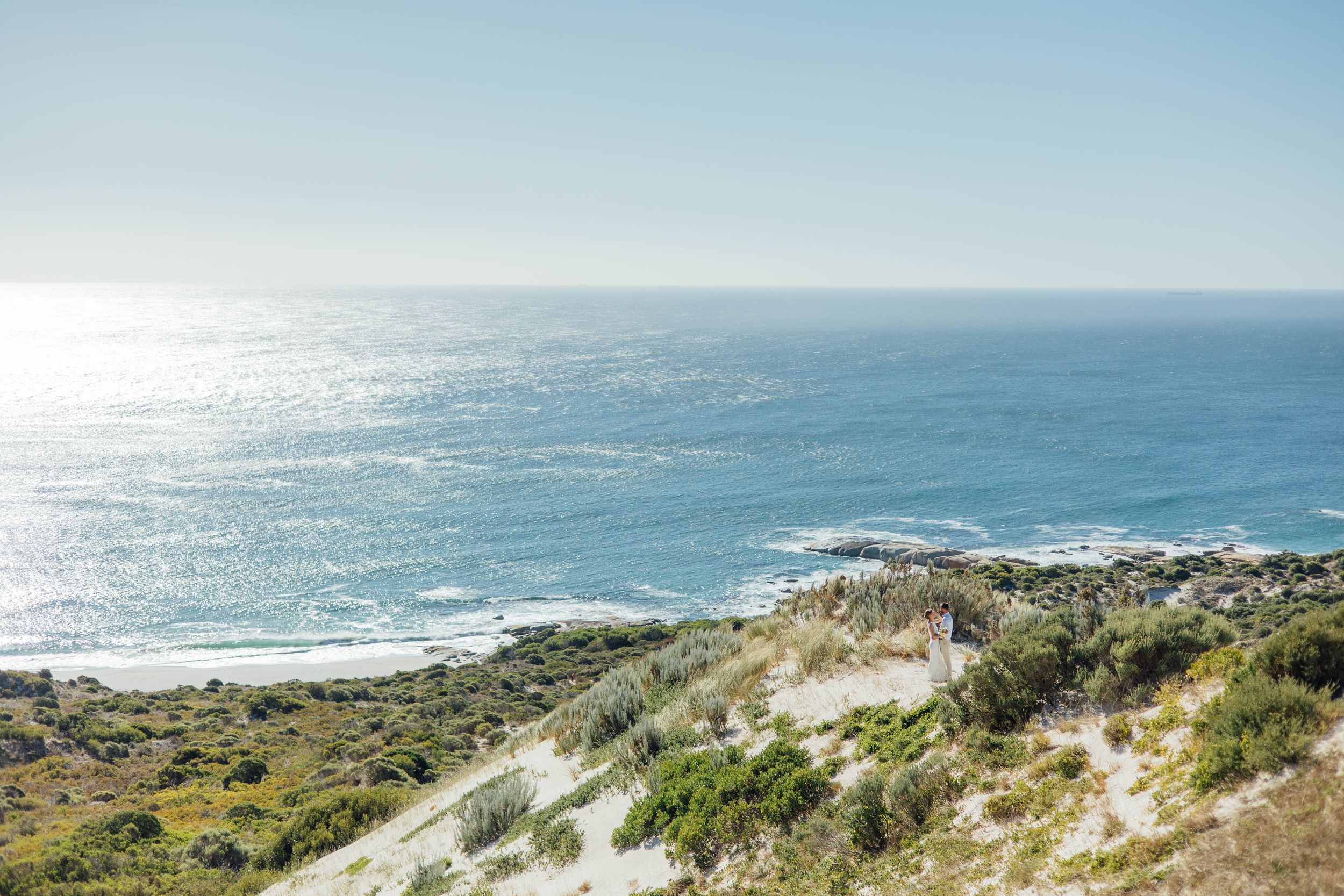 Scenic coastal landscape with sandy dunes and blue ocean waters reflecting sunlight on a clear day.