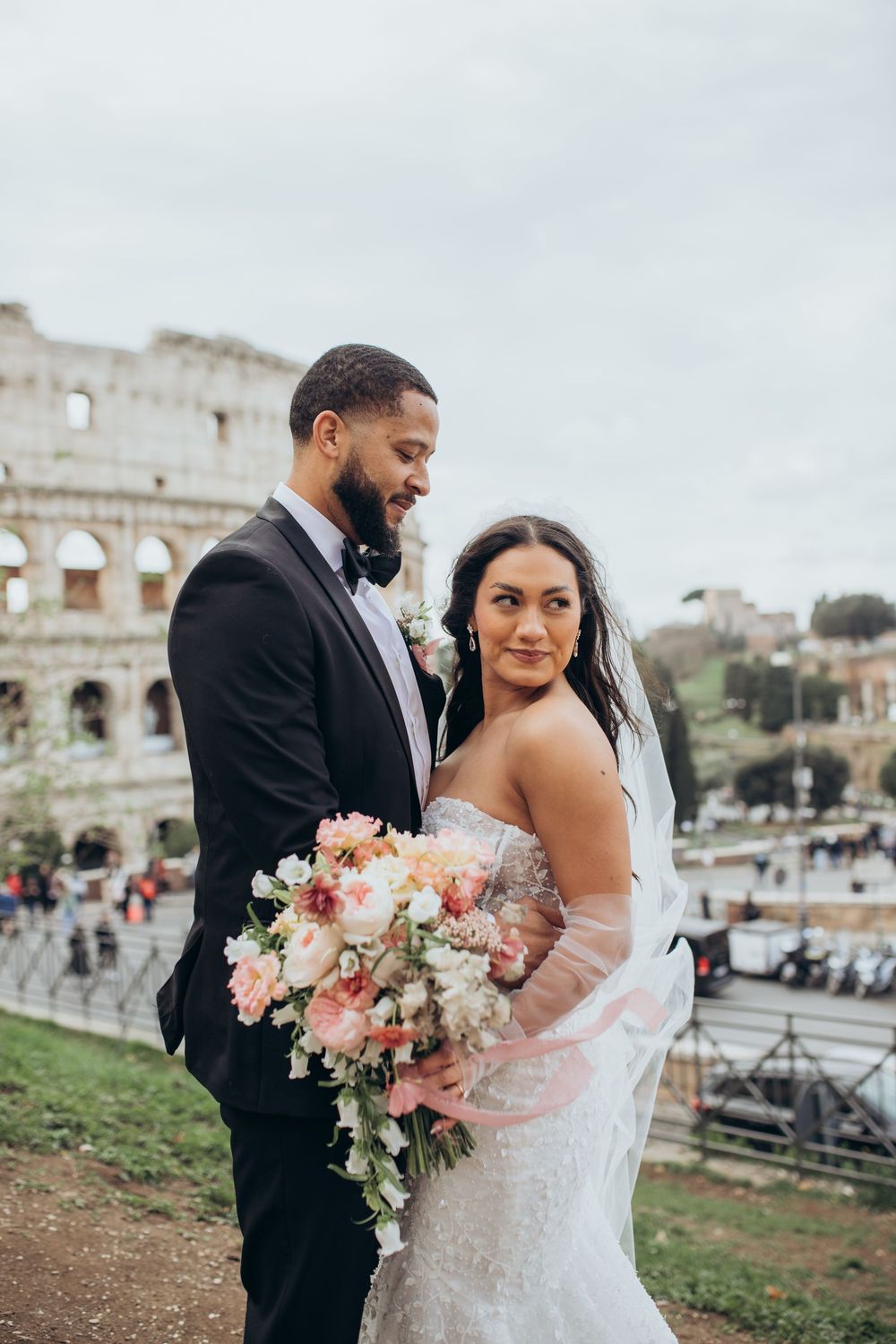 Bride holds beautiful pink bouquet while posing with groom at the Colosseum in Rome.