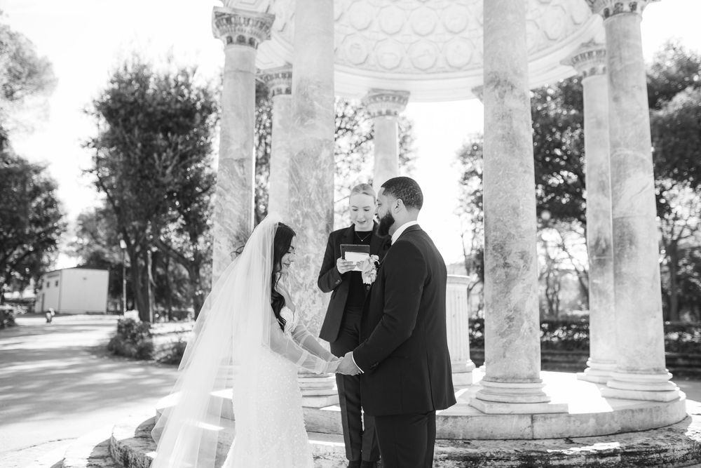 Black and white photo of a wedding ceremony under a columned gazebo with a bride in flowing veil.