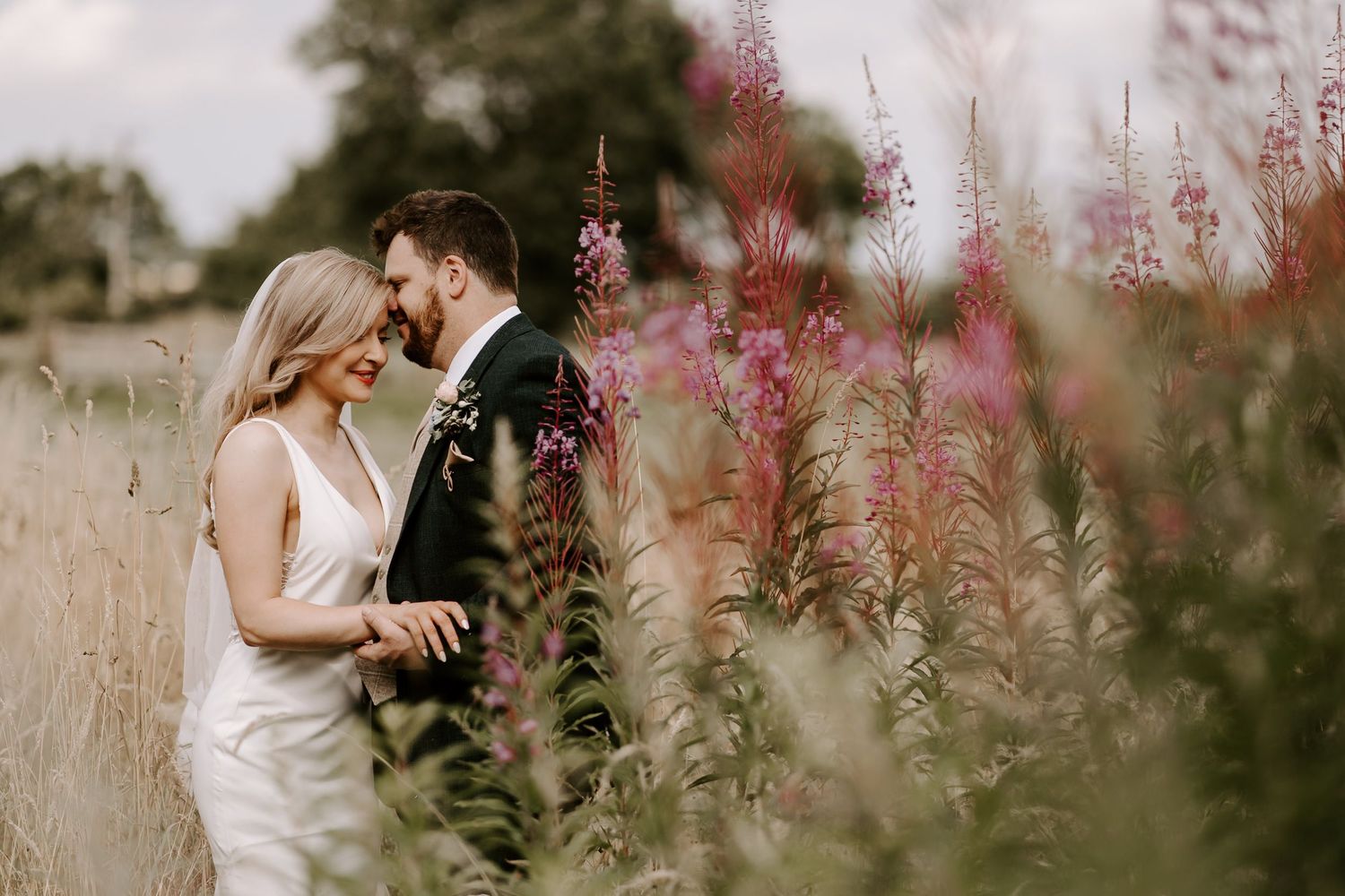 A couple embraces in a field of pink fireweed flowers on their wedding day.