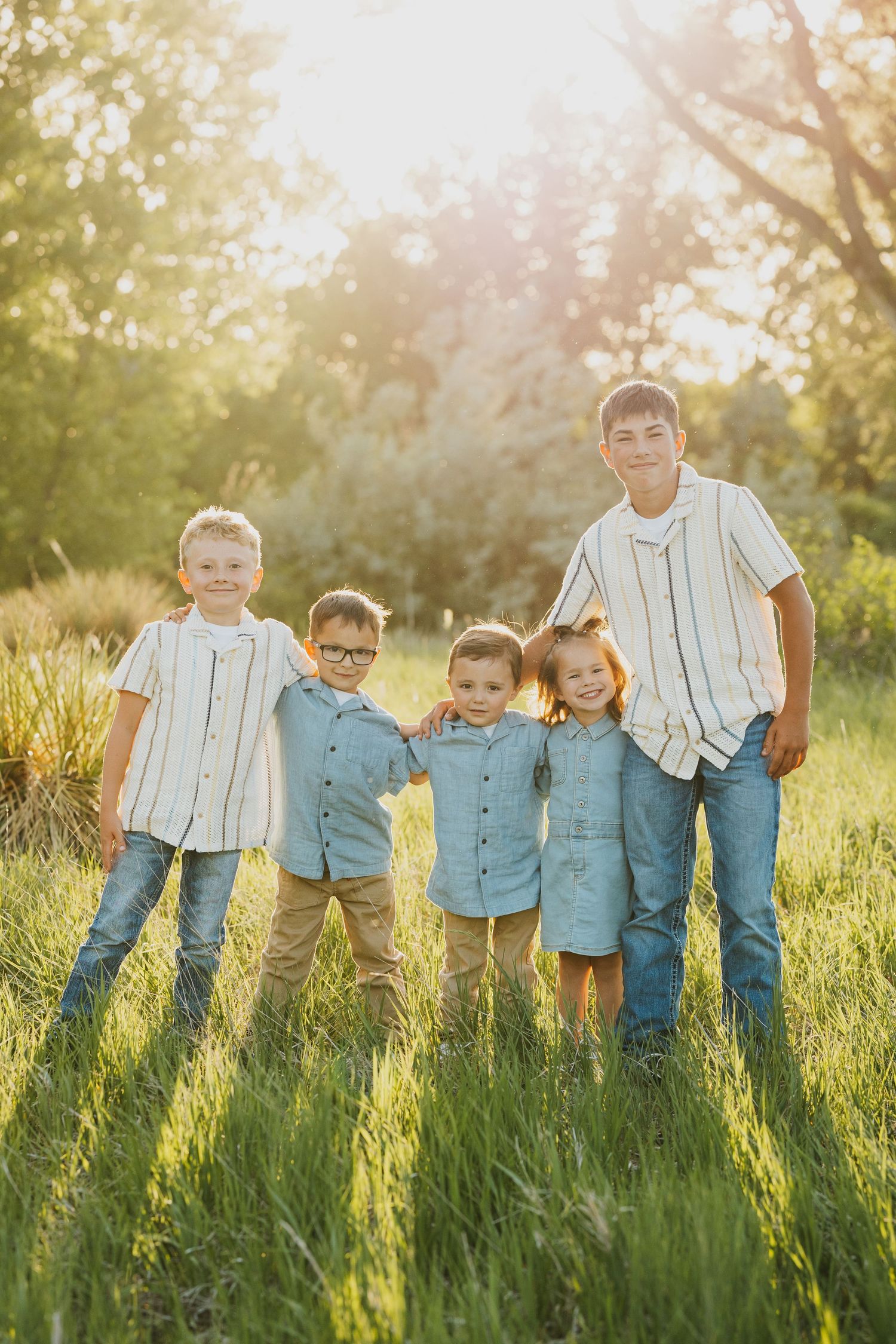 A casual family photoshoot on a grassy hillside during golden hour.