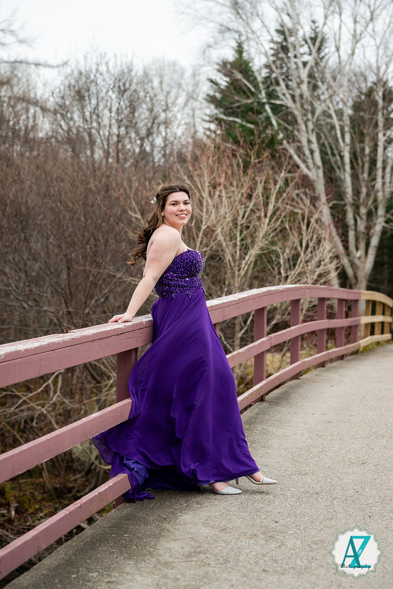 An elegant purple ball gown creates a striking contrast against a rustic wooden bridge in nature.
