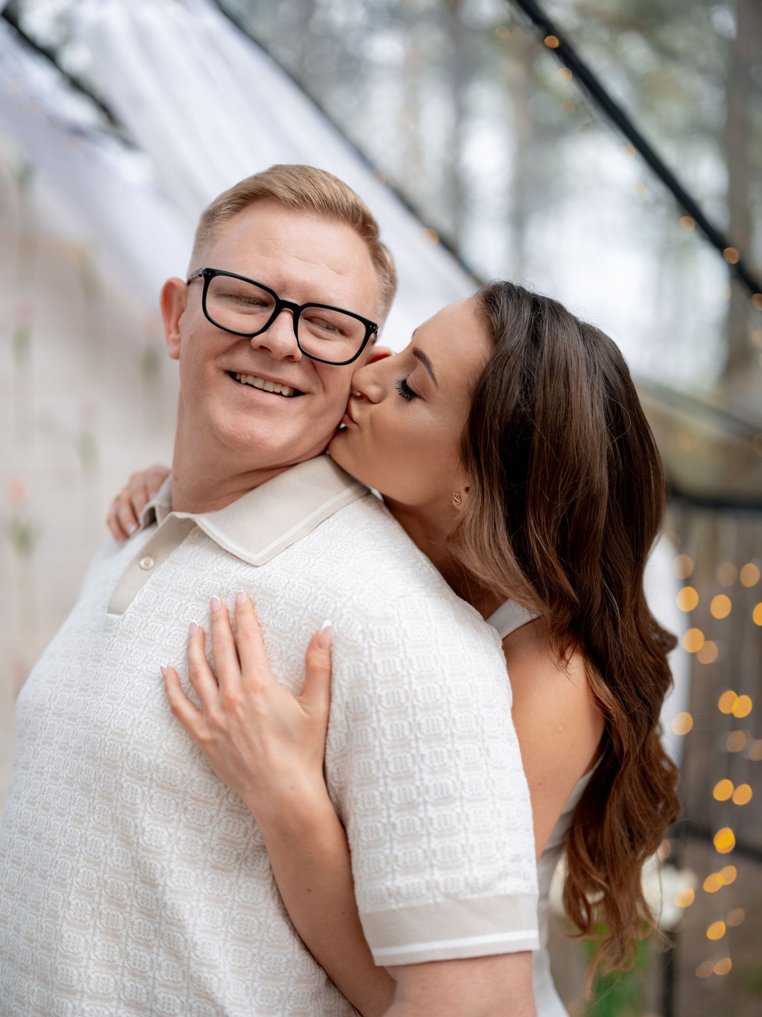 A romantic couple embraces outdoors with bokeh lights in the background during a tender moment.