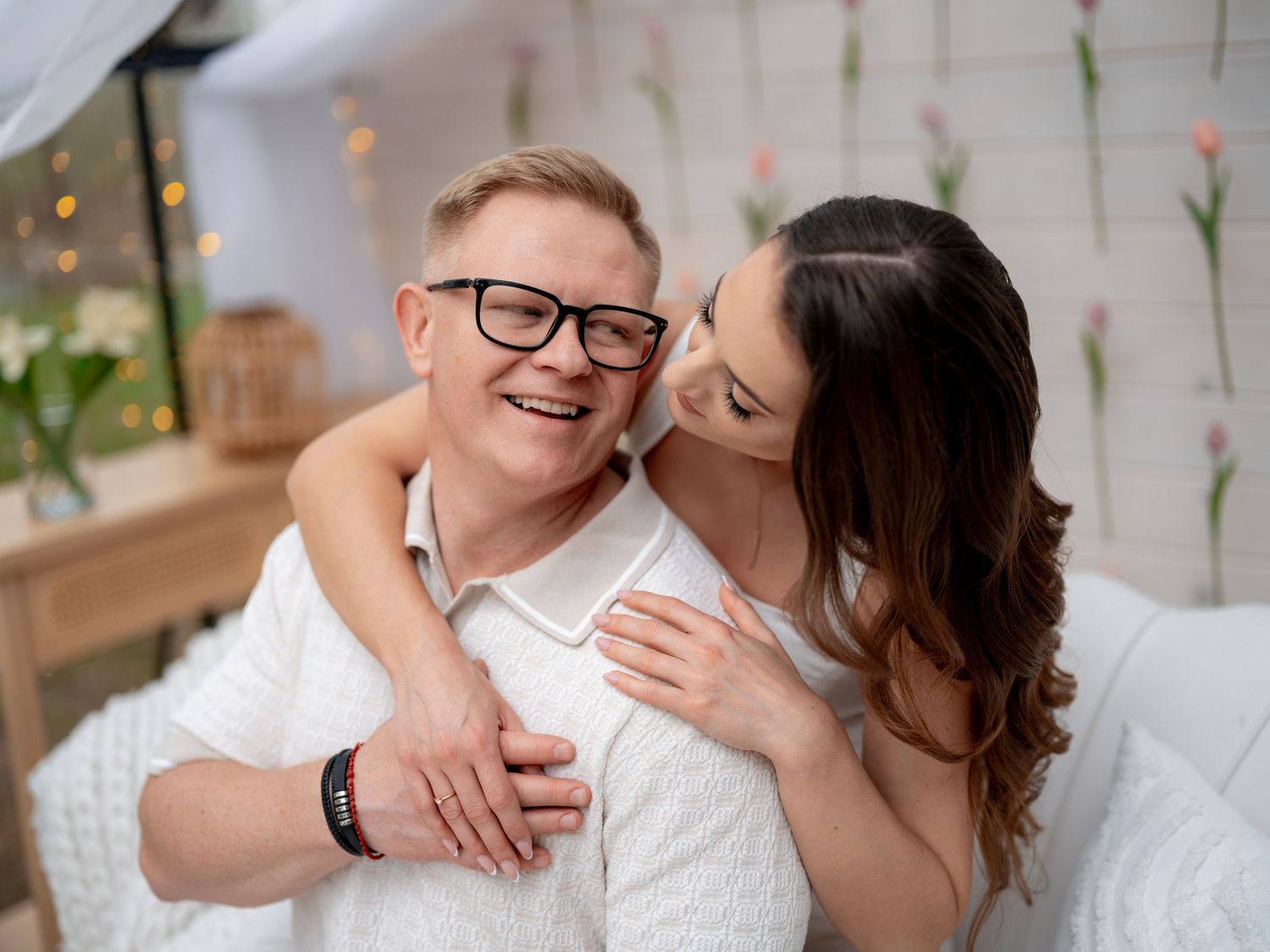 A loving couple shares an intimate moment together while relaxing on a couch with floral decorations in the background.