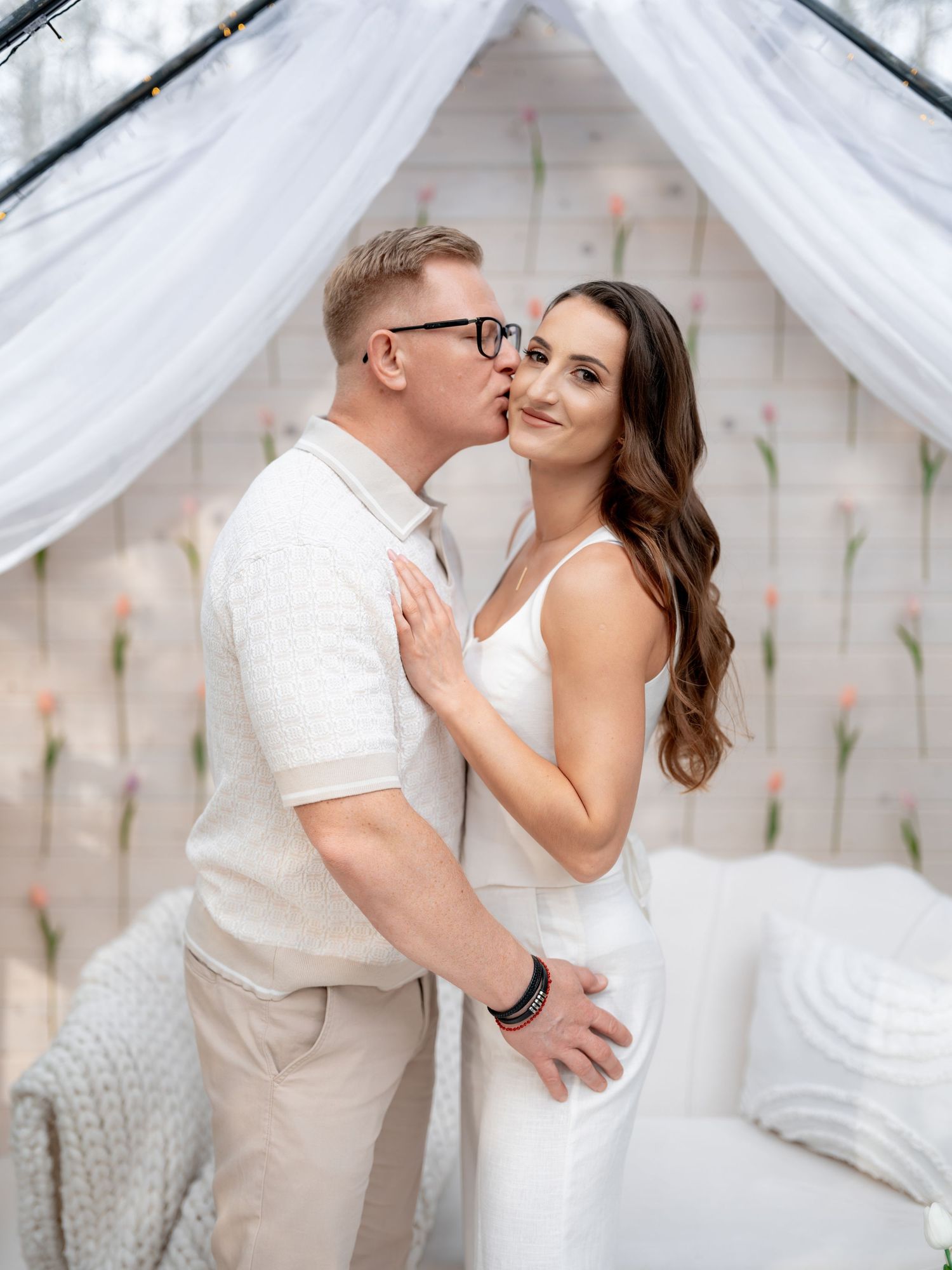 Intimate moment between couple under white canopy with soft lighting and decorative backdrop.