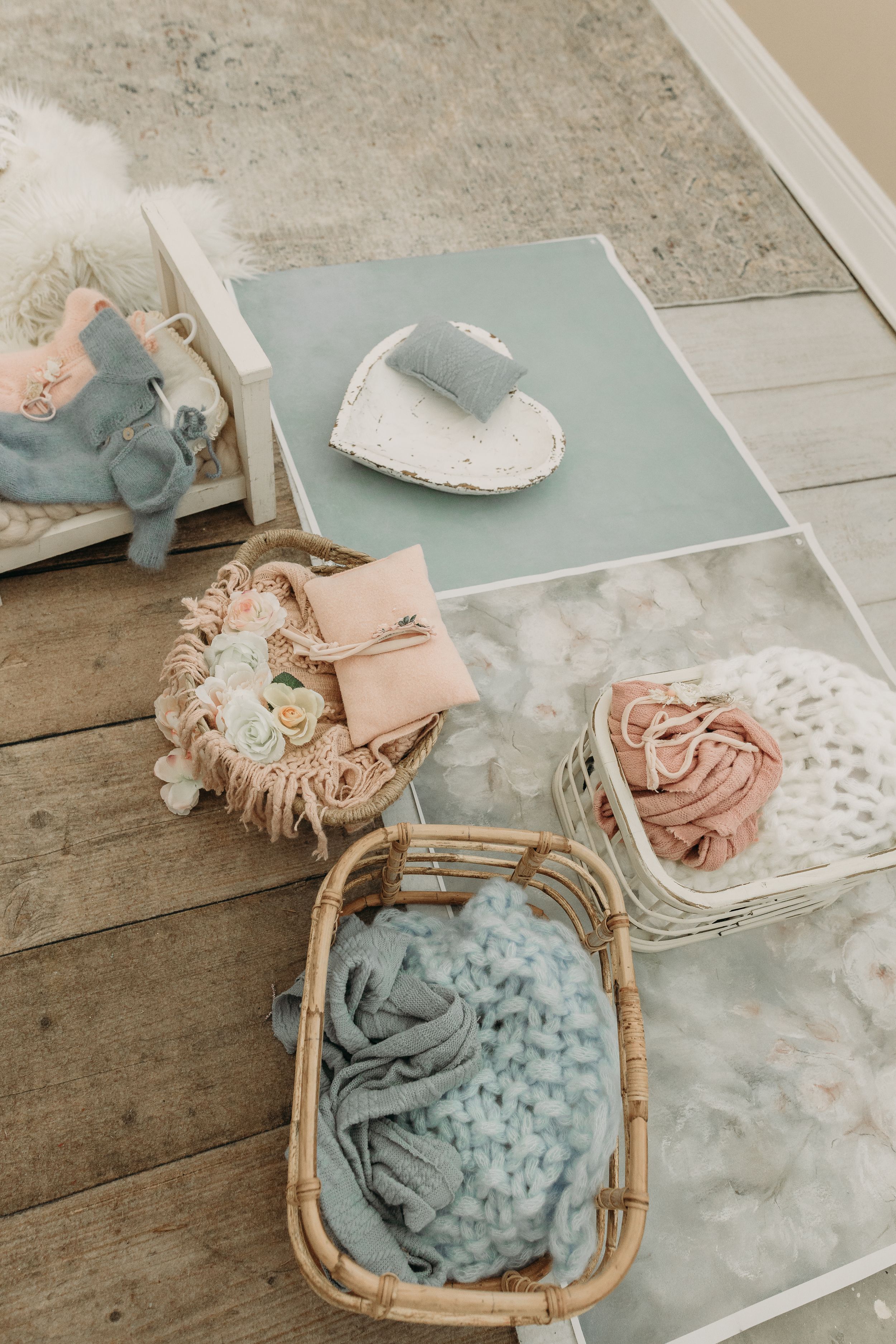 Soft pastel baby accessories including a wicker basket, blanket, shoes and decorative items in muted blue and pink tones.