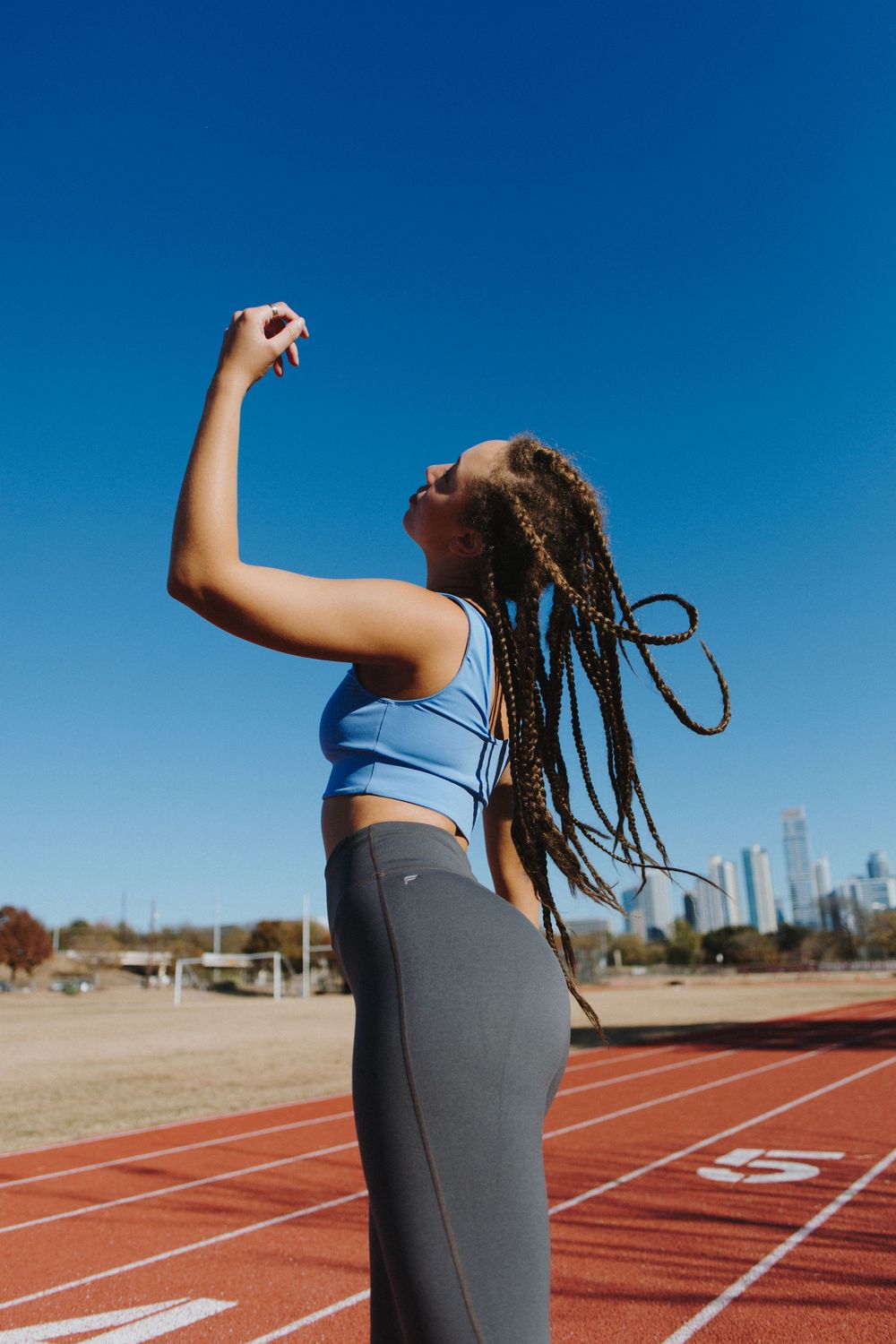 Athlete stretching on a running track against bright blue sky.