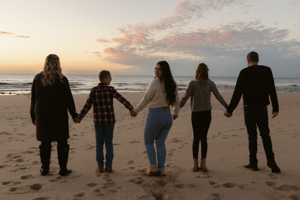 Silhouetted group holding hands while walking along a beach at sunset.
