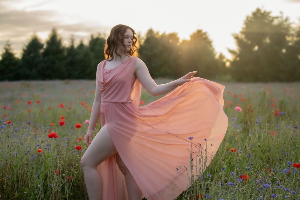 Person in flowing pink dress twirls in field of wildflowers at sunset.