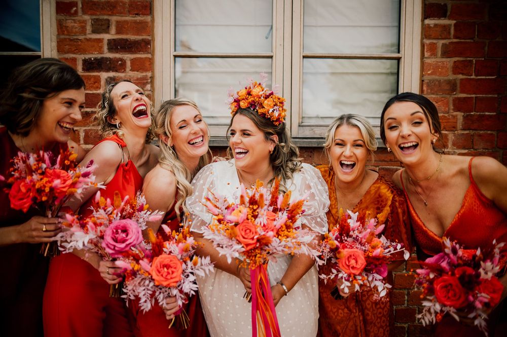 Group celebrates with bright coral flowers against a brick wall background. Worcestershire Wedding photographer.