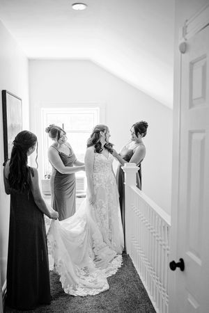 Bride and bridesmaids preparing in hallway, black and white wedding photo with elegant lace gown.
