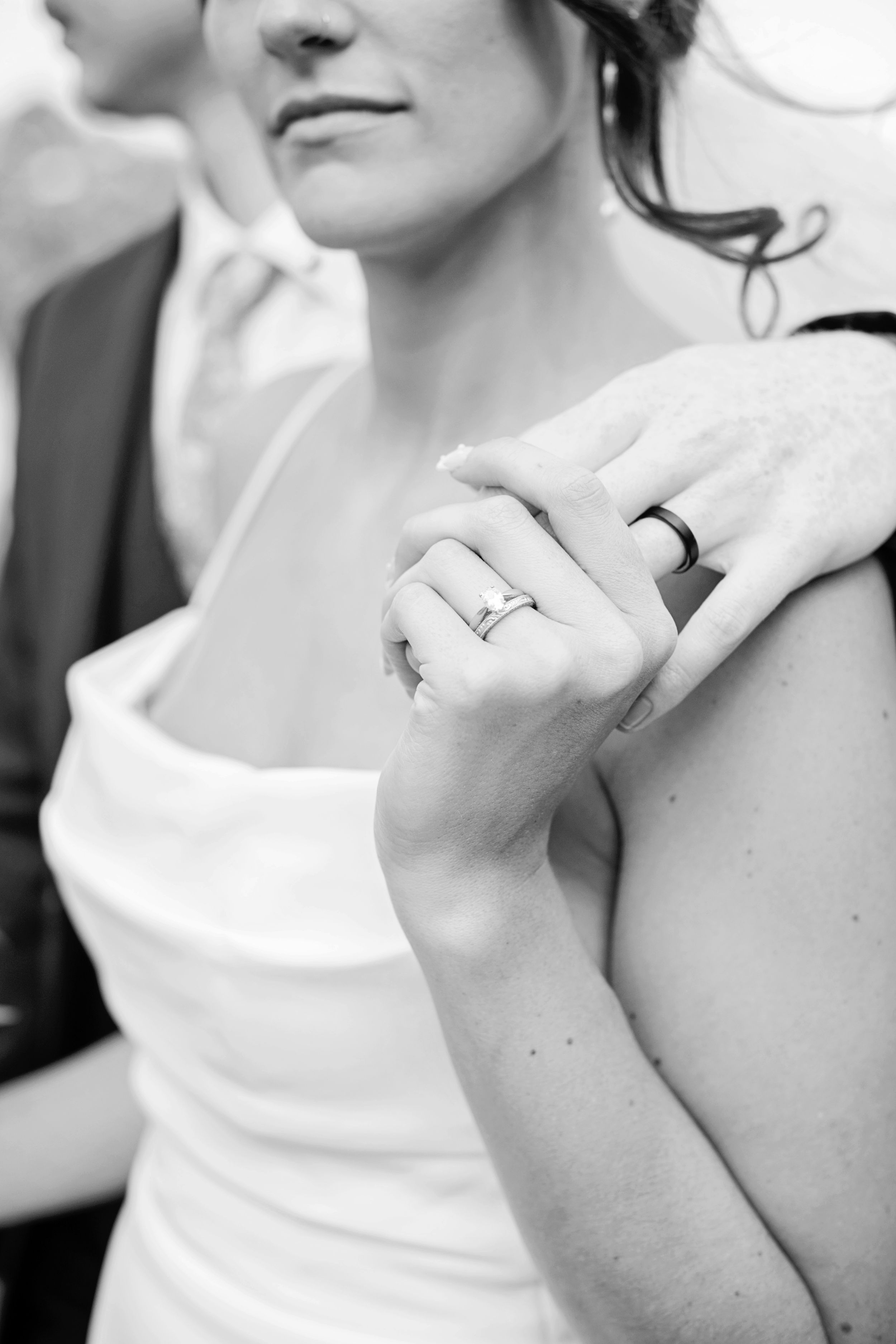 Close-up black and white photo of bride and groom wedding rings on clasped hands.