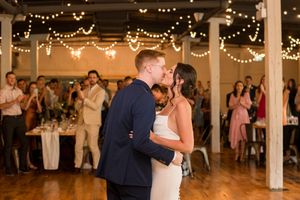 Bride and groom sharing their first dance under warm string lights surrounded by wedding guests.