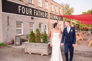 Bride and groom walking hand in hand outside Four Fathers Brewing Co. on their wedding day.